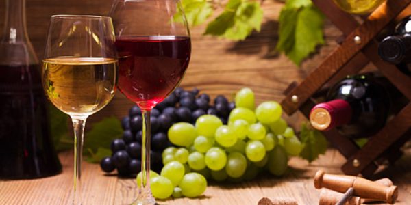 Glasses of red and white wine, served with grapes on a wooden background